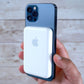 Hand holding a smartphone with a white MagSafe charger against a light wooden background