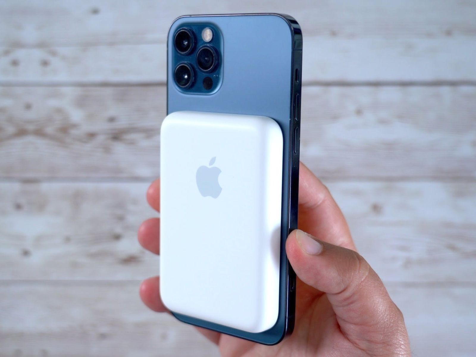 Hand holding a smartphone with a white MagSafe charger against a light wooden background